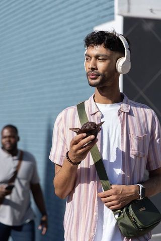 Indian man in 20s walking with headphones holding chocolate muffin urban lifestyle portrait