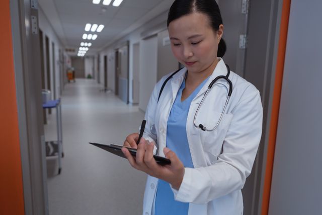 Front view of female doctor writing on clipboard in corridor at hospital