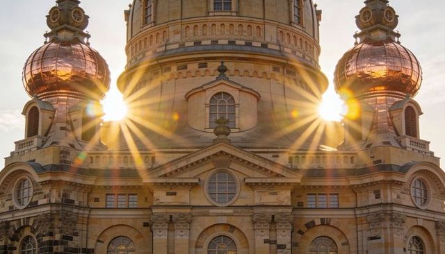 Sunburst through copper cupolas of historic baroque dome over ornate stone facade