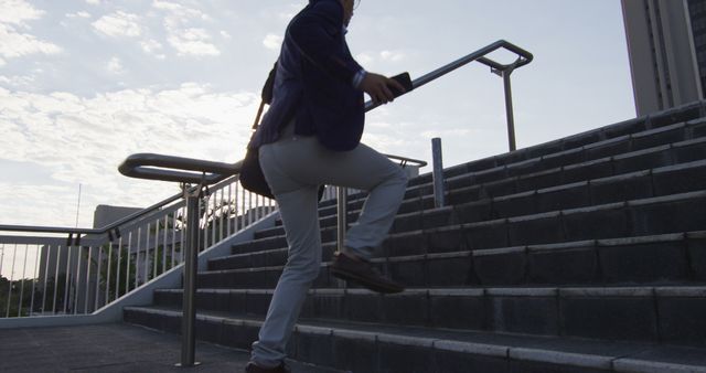 Businessperson climbs stairs outdoors in morning sunlight wearing professional attire, heading to work or a meeting with a backpack. This image can be used for business, motivation, professional life, urban commute, determination, and city life themes.