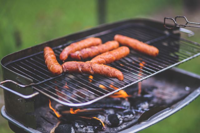 Close-up view of multiple sausages grilling on charcoal barbecue grille, outdoor picnic, ideal for summer, backyard barbecue party, allows you to capture the essence of outdoor cooking and casual gatherings.