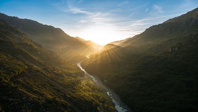 Sunburst bathing alpine valley in golden light over winding river and farm lands