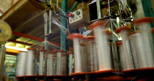 Spools of thread are rapidly spinning on industrial textile machinery, capturing the dynamic environment of a fabric manufacturing plant. Machinery like this plays a crucial role in the mass production of textiles for various applications.