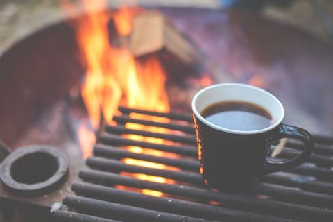 Campfire coffee mug sitting on grill over glowing flames, cozy outdoor morning beverage