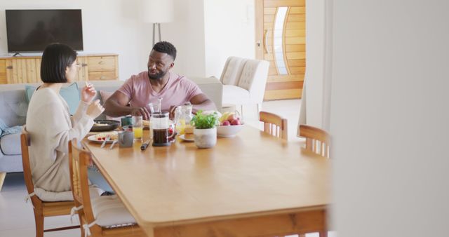 Happy diverse couple sitting at table and having breakfast. Spending quality time at home concept.