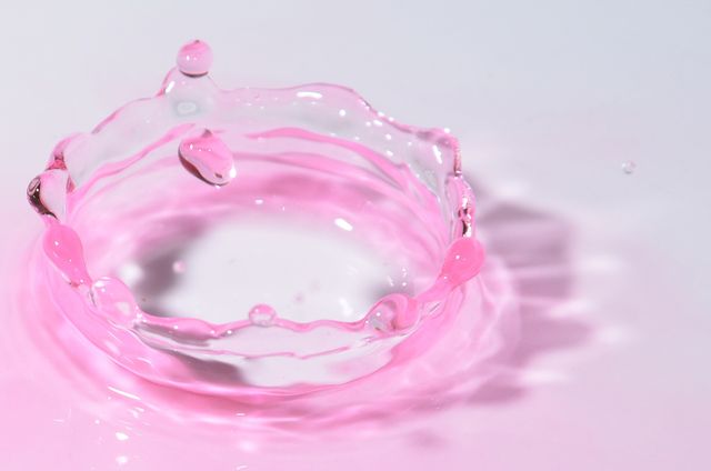 This visually captivating image showcases a pink water drop creating a splash with ripples extending outward. Ideal for use in design projects focused on fluid dynamics, water conservation, or environmental themes. Perfect for websites, advertisements, presentations, or artistic contexts requiring a blend of abstract art and vibrant color appeal.