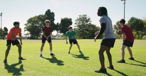 Multiracial male athletes practicing agility and passing drills on park field