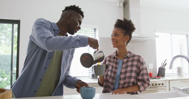 Couple enjoying morning coffee in a modern kitchen while smiling and interacting. Bright, clean space with modern appliances and natural light. Ideal for advertising kitchen products, coffee brands, or promoting a relaxed, happy lifestyle.