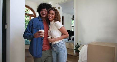 Happy couple moving into new home embracing with coffee
