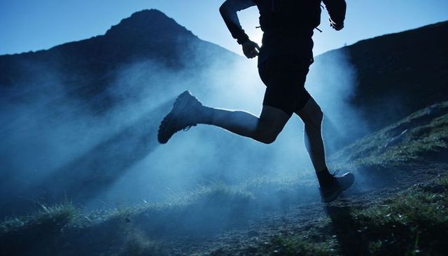 Trail runner sprinting on misty alpine ridge backlit by dramatic blue dawn light for endurance