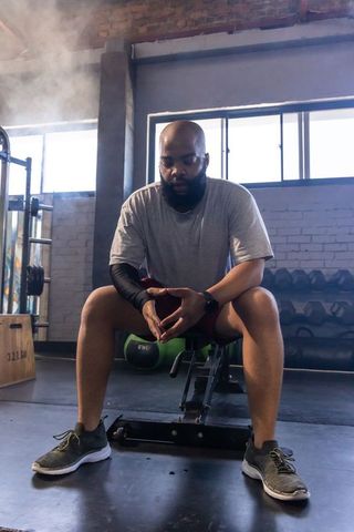 African man resting on weight bench in moody industrial gym focused post-workout recovery
