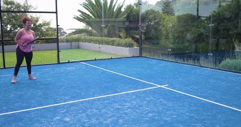 African american woman playing padel on bright blue residential court holding racket
