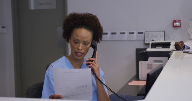 Biracial hospital worker in reception talking on phone with doctors in backgrund - Download Free Stock Photos Pikwizard.com