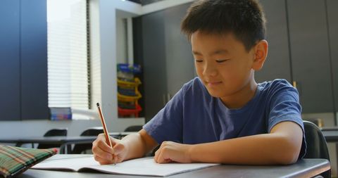 Focused Asian Schoolboy Writing in Classroom Setting - Download Free Stock Images Pikwizard.com