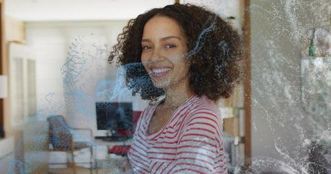 Smiling woman wearing red striped shirt standing behind soapy glass in cozy living room