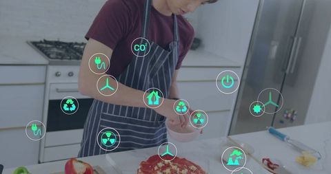 Korean cook preparing pizza with augmented reality sustainability icons in modern kitchen