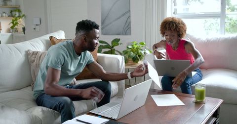 Couple collaborating on laptops, sharing documents across living room table for home office