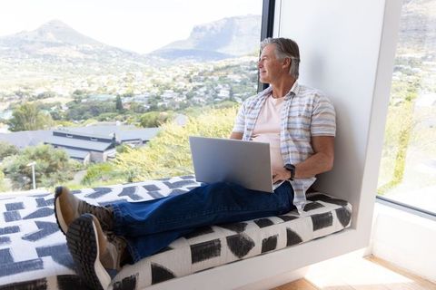 Mature man working on laptop in bright window seat with panoramic mountain and valley view