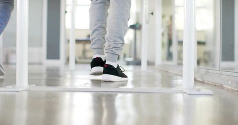 Adult male walking in dance studio wearing grey sweatpants black sneakers by barre