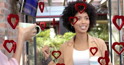 Young woman chatting at outdoor cafe holding takeaway cup with floating red hearts