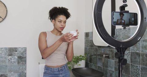 African american woman recording skincare tutorial at bathroom vanity with ring light
