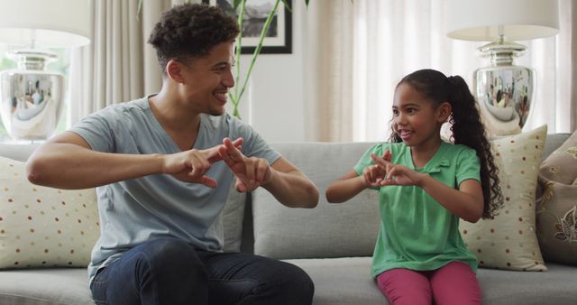 Happy biracial father and daughter sitting on sofa using sign language. domestic lifestyle, spending free time at home.
