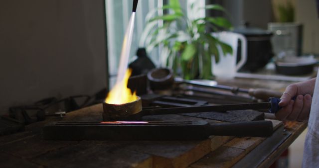 Blacksmith heating metal in workshop using open flame with tongs on workbench. Capture suitable for industry, craftsmanship, and working process-related projects. Perfect for representing traditional metalworking skills and artisans.