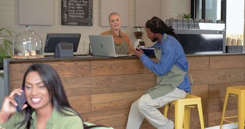 African american man seated at cafe counter using phone while barista smiles behind laptop