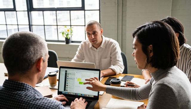 Team Collaborating Over Laptop in Bright Urban Office Pointing at Screen During Meeting