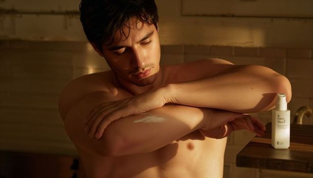 Applying moisturizer during golden hour sunlit shirtless man rubbing lotion on forearm