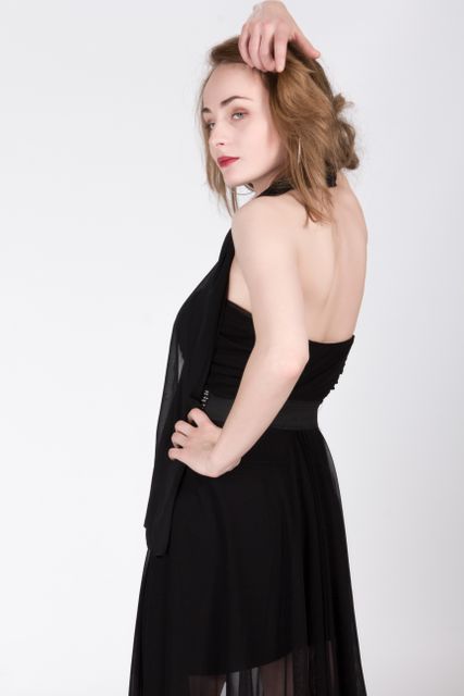 Elegant woman posing in a chic black dress with her hand resting on her head. Perfect for fashion magazines, style blogs, and clothing brand promotions, highlighting elegance and confidence.