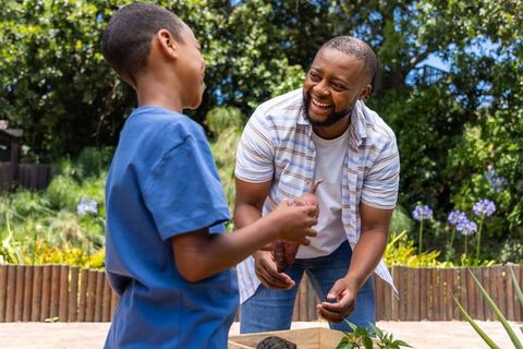 African father and son harvesting sweet potatoes together in vibrant backyard garden