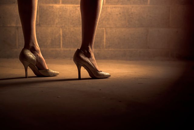 Silhouette of woman's legs in high heels with warm lighting, highlighting elegance and style. Perfect for use in fashion editorials, glamour magazines, lifestyle blogs, or advertisements focusing on evening wear, footwear, or feminine chic.