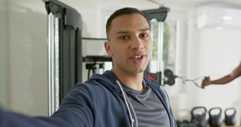 African american man recording workout selfie in bright fitness studio with kettlebells