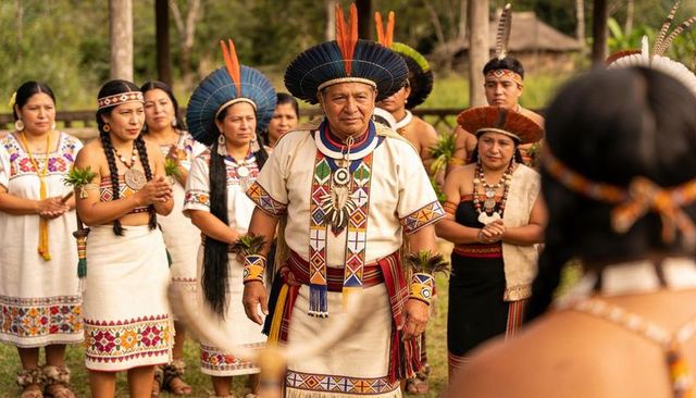 Indigenous elder leading ritual with feather headdress and embroidered ceremonial tunic