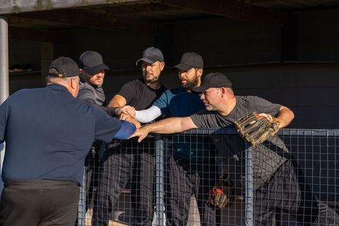 Baseball team sharing pregame fist bump in dugout over fence showing unity and focus
