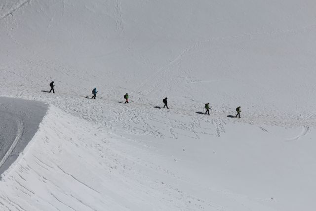 Team of hikers trekking across a snowy mountain ridge in winter. Ideal for topics on adventure travel, outdoor activities, teamwork, winter sports, and challenges. Perfect for use in travel blogs, sports magazines, adventure gear marketing, and motivational content.