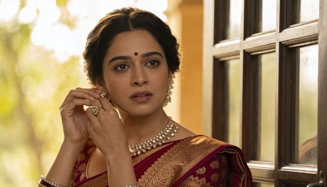 Indian woman adjusting earring wearing maroon saree with gold border and pearl necklace
