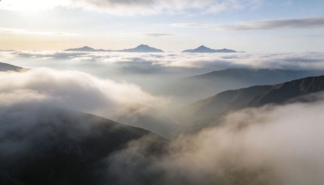 Sunlit Mountain Ridge Cutting Through Rolling Mist at High Alpine Sunrise Panorama