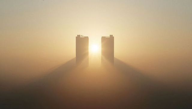 City sunrise with skyscrapers emerging from thick fog