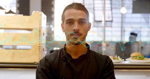 Young chef standing confidently in modern kitchen presenting plated burgers and salads