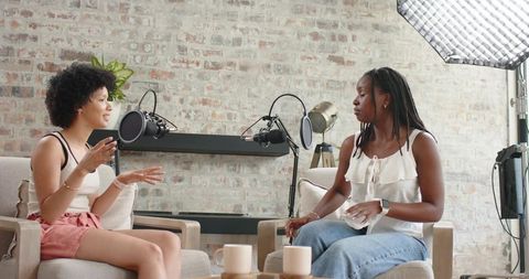 African american women recording podcast and chatting in cozy brick studio with microphones