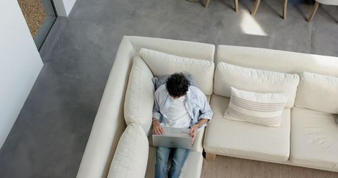 Man working on laptop from home on stylish beige sofa