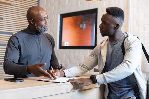 Mature staff explaining while african american visitor signing form at reception desk