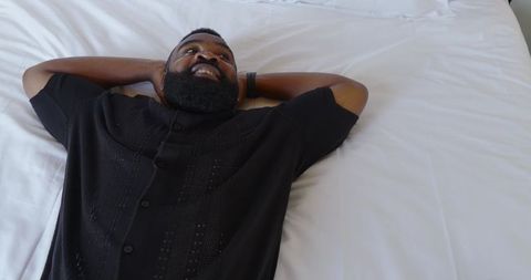 African American Man Relaxing Gleefully on Comfortable White Bedding
