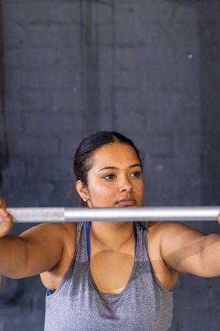 Asian woman gripping straight bar, focusing on strength training and weightlifting form