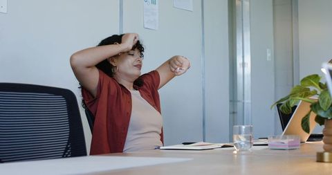 African american woman stretching at conference table with laptop notebook and plant