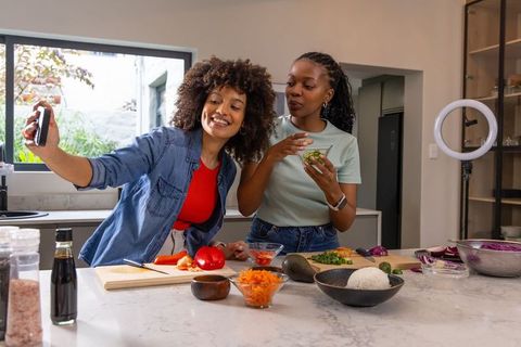 African American friends recording cooking video and tasting recipe at kitchen island