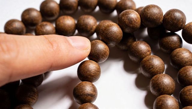 Finger rolling over wooden prayer beads showing grain texture and tactile detail