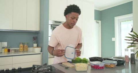 African american man meal-prepping on modern kitchen island sealing containers for weekly lunches